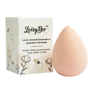 May include: A pink, teardrop-shaped makeup sponge made from sugarcane and corn flour. The sponge is packaged in a white box with a bee illustration and the text "Luley Bee 100% Biodegradable Makeup Sponge Made from Sugarcane, and Corn Flour."