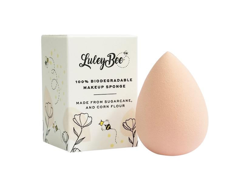 K&ouml;nnte beinhalten: Ein rosa, tropfenf&ouml;rmiger Make-up-Schwamm aus Zuckerrohr und Maisst&auml;rke. Der Schwamm ist in einer wei&szlig;en Box mit einer Bienenillustration und dem Text "Luley Bee 100% Biologisch abbaubarer Make-up-Schwamm Hergestellt aus Zuckerrohr und Maisst&auml;rke." verpackt.