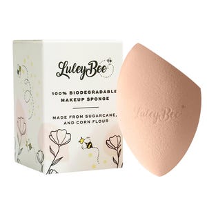 May include: A peach-colored makeup sponge next to a white box. The box has the text "Luley Bee" and "100% Biodegradable Makeup Sponge" with illustrations of bees and flowers. The sponge is made from sugarcane and corn flour.