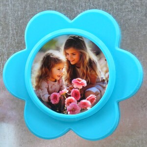 May include: A blue flower-shaped photo frame with a picture of two girls in a garden with pink flowers.
