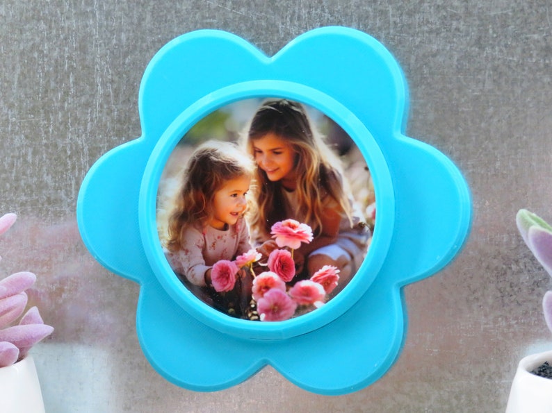 May include: A blue flower-shaped photo frame with a picture of two girls in a garden with pink flowers.