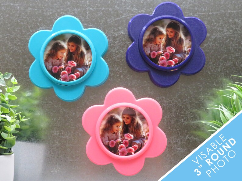 May include: Three flower-shaped photo frames in blue, pink, and purple, each with a 7.6 cm round photo insert. The photos show two young girls smiling and looking at flowers.