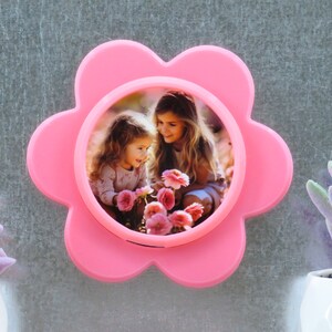 May include: A pink flower-shaped photo frame with a picture of two girls smiling and holding flowers.