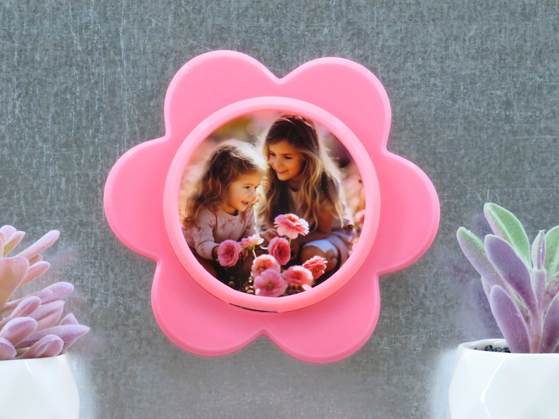 May include: A pink flower-shaped photo frame with a picture of two girls smiling and holding flowers.