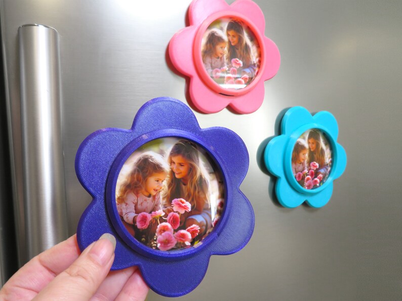 May include: Three flower-shaped photo frames with magnets on the back. The frames are pink, blue, and purple. Each frame has a photo of two girls looking at flowers.