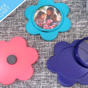 May include: Three 5x5 inch flower-shaped magnets. One is blue with a photo of two girls in the centre. One is pink with a black magnet on the back. One is purple with a clear magnifying glass on top.