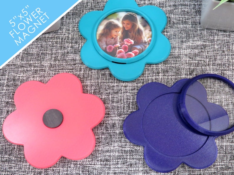 May include: Three 5x5 inch flower-shaped magnets. One is blue with a photo of two girls in the centre. One is pink with a black magnet on the back. One is purple with a clear magnifying glass on top.