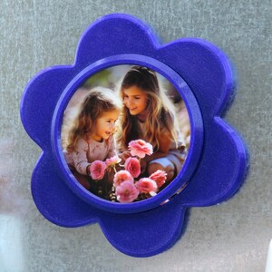 May include: A blue flower-shaped photo frame with a picture of two girls smiling and holding pink flowers.