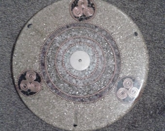 May include: A round, white, decorative plate with a silver and white center and three copper wire triquetras around the edge.