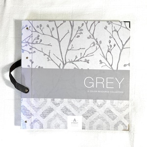 May include: A square sample book titled GREY A COLOR RESOURCE COLLECTION by A STREET PRINTS. The cover features a top section with grey branches on a white background, a solid grey center band, and a bottom section with a grey geometric pattern.