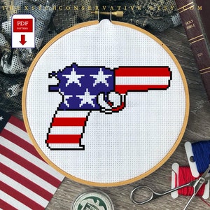 May include: Cross stitch pattern of a gun with the American flag design. The pattern is in a wooden embroidery hoop. The hoop is on a wooden surface with a bible, scissors, and embroidery floss.