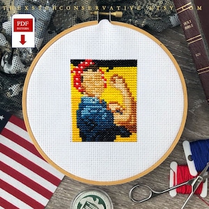 Puede incluir: Un aro de bordado de punto de cruz con un fondo de tela blanca. El bordado representa a una mujer con una bandana roja, vistiendo una camisa azul y levantando su puño derecho en el aire. El fondo es amarillo.