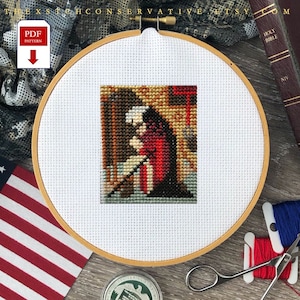 Puede incluir: Un patrón de punto de cruz de una mujer con un vestido rojo arrodillada en oración. El patrón se muestra en un aro de bordado de madera. El aro está sobre una superficie de madera con una bandera de Estados Unidos, una Biblia y hilo de bordar.