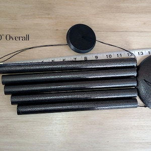 May include: A black wind chime with five cylindrical tubes and a circular top piece. A round hanging plaque features the letter R and the text Welcome to Our Home. A measuring tape is visible, and text indicates 30 inches overall length.