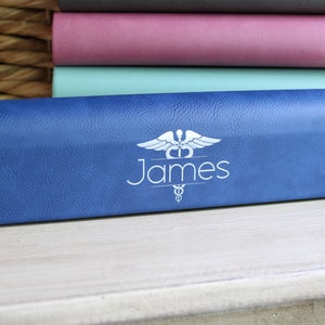 May include: A blue leather eyeglasses case with a white medical symbol and the name "James" printed on it.