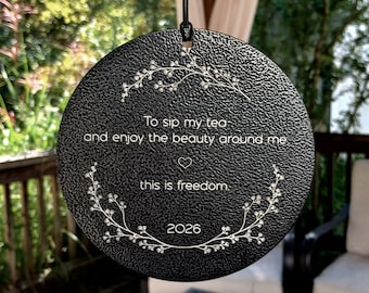 May include: A round black hanging ornament with a textured surface featuring white engraved text that reads: To sip my tea and enjoy the beauty around me, this is freedom. It includes a small heart icon and the year 2026.