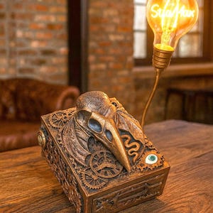 Puede incluir: Caja decorativa de estilo steampunk con una calavera de pájaro y detalles de engranajes. Una bombilla iluminada con el texto "Star Max" está adjunta. La caja, de metal color bronce, se encuentra sobre una superficie de madera.