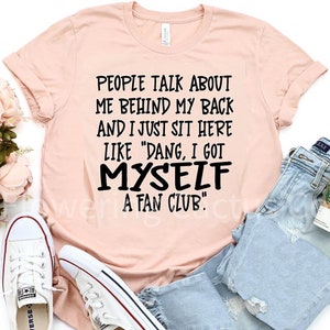 May include: A peach-colored t-shirt with black text that reads "People talk about me behind my back and I just sit here like "Dang, I got myself a fan club."