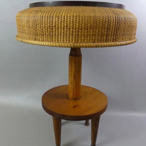 May include: A vintage side table featuring a woven rattan top with a dark brown rim. The table has a wooden stem and a round base with three legs. The table is made of light brown wood and has a classic design.