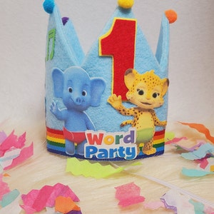 May include: Blue felt crown with a red number one, a rainbow ribbon, and images of characters from the show Word Party. The crown has yellow and orange pom-poms on the top.