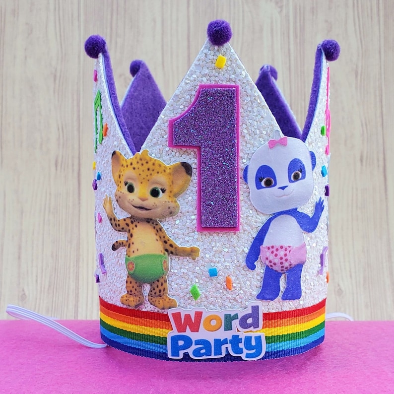 Puede incluir: Corona de cumplea&ntilde;os de color morado y blanco con un borde de arco&iacute;ris. La corona presenta un gran n&uacute;mero 1 morado, un personaje de guepardo y un personaje de panda. El texto "Word Party" est&aacute; impreso en la corona.