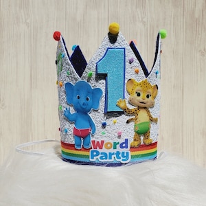 Puede incluir: Una corona de fieltro blanco con una base de fieltro azul, que presenta un n&uacute;mero uno azul, un elefante azul y un guepardo amarillo. La corona tiene una cinta de arco&iacute;ris y las palabras "Word Party" en letras amarillas y naranjas.