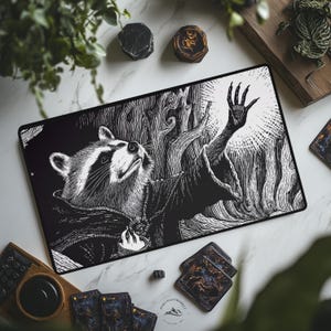 May include: Black and white illustration of a raccoon in a cloak, reaching towards a bright light. The artwork is on a rectangular mat, with a black border. The scene includes stylized trees and a hand with long fingers. The mat is surrounded by other items.