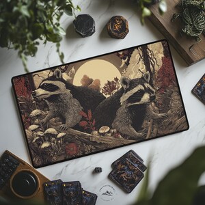 May include: A rectangular mousepad featuring a detailed illustration of two raccoons in a forest setting, with a full moon in the background. The color palette includes shades of brown, gray, and cream. The mousepad is surrounded by other items, including coasters and a wooden tray.