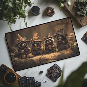 May include: A rectangular mousepad features an illustration of four raccoons wearing wizard hats and cloaks, each holding a small book. The artwork is set in a forest with a warm color palette. Additional items include coasters and a deck of cards.