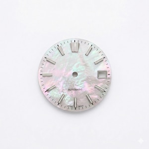 May include: A watch face with a pearlescent, iridescent finish. The face features silver-toned hour markers and hands, with the word "AUTOMATIC" printed in the center. The text "JAPAN MOVT" is printed at the bottom. The watch face has a date window.