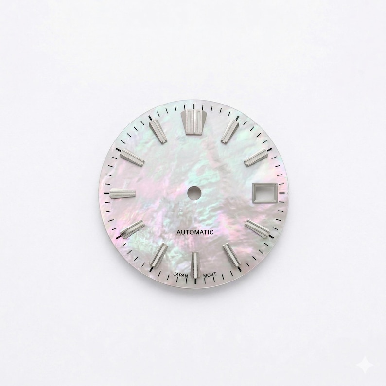 May include: A watch face with a pearlescent, iridescent finish. The face features silver-toned hour markers and hands, with the word "AUTOMATIC" printed in the center. The text "JAPAN MOVT" is printed at the bottom. The watch face has a date window.