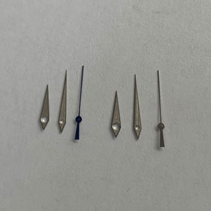 May include: A set of six watch hands, including a blue hour hand, a silver minute hand, a silver second hand, and three silver hands for a watch with a date complication.
