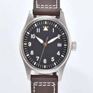 May include: A stainless steel wristwatch with a black face, white numerals, and a date display at the 3 o'clock position. The watch has brown leather straps with white stitching. The watch face has a triangle at the 12 o'clock position.