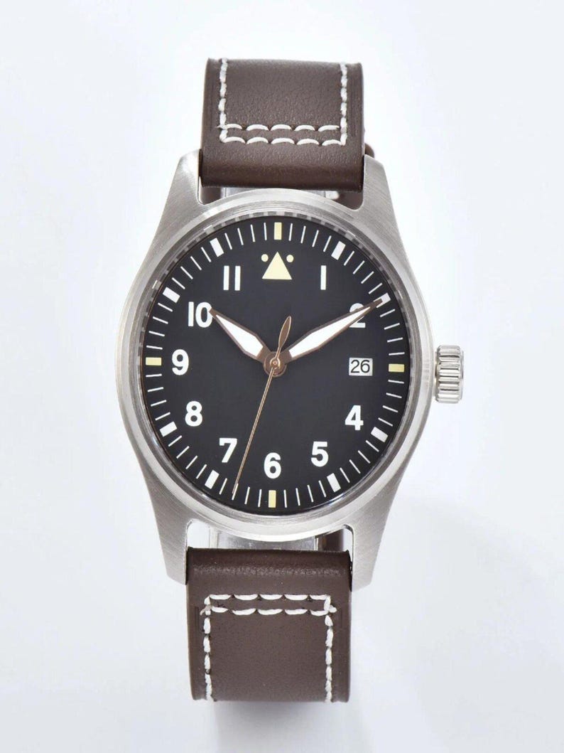 May include: A stainless steel wristwatch with a black face, white numerals, and a date display at the 3 o'clock position. The watch has brown leather straps with white stitching. The watch face has a triangle at the 12 o'clock position.