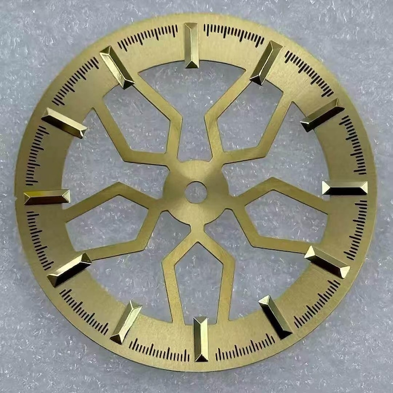 Pode incluir: Mostrador de rel&oacute;gio dourado com um design geom&eacute;trico complexo. Possui marcadores retangulares e linhas finas para medi&ccedil;&atilde;o do tempo. O centro tem um orif&iacute;cio e o design &eacute; intrincado e detalhado.