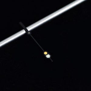 May include: Close-up of a watch face with a black background. The watch hands are black with a yellow and white luminous dot. A silver metal bar is in the upper left corner.