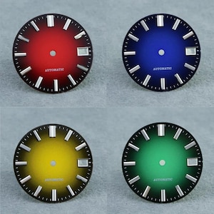 May include: Four circular watch dials in red, blue, yellow, and green, each featuring a gradient finish, silver-toned hour markers, a central hole for hands, and a date window at the three o'clock position with the word AUTOMATIC printed below.