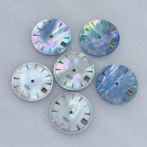Puede incluir: Seis esferas de reloj con caras iridiscentes de n&aacute;car. Las esferas presentan agujas y marcadores plateados, con el texto "PRESAGE AUTOMATIC" impreso en la mitad inferior. Las esferas son en tonos de azul, blanco y colores iridiscentes.