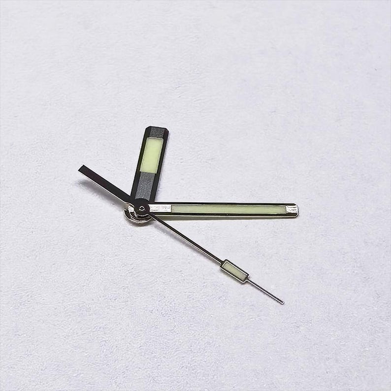 May include: Watch hands set, featuring a black and silver design with luminous green accents. The hour hand is a rectangular shape, the minute hand is a long rectangle, and the second hand is a thin line with a small rectangle.
