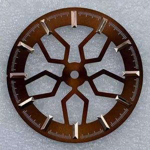Pode incluir: Um mostrador de rel&oacute;gio castanho com um design geom&eacute;trico e marcadores de hora dourados. O mostrador tem formato circular com formas recortadas e uma pista de minutos. Os marcadores de hora s&atilde;o retangulares e ligeiramente elevados.
