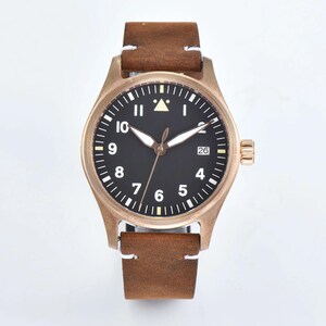 May include: A bronze-colored wristwatch with a black face and white numerals. The watch has a brown leather strap with white stitching. The watch face displays the date and has luminous hands. The watch case is approximately 40mm in diameter.