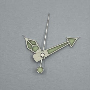 May include: Close-up of watch hands on a gray background. The hands are silver with a luminescent green fill. The hour hand is a stylized arrow, the minute hand is a long, thin pointer, and the second hand has a circular end.