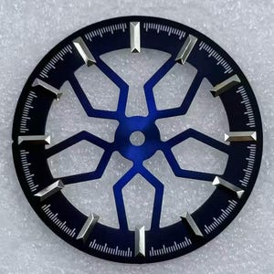 Pode incluir: Um mostrador de rel&oacute;gio com um mostrador azul escuro e um design geom&eacute;trico azul mais claro no centro. Marcadores de hora prateados est&atilde;o presentes. A borda externa tem uma faixa de minutos com pequenas linhas.