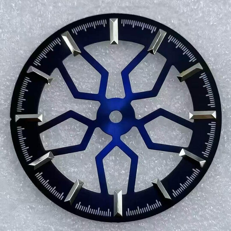 Pode incluir: Um mostrador de rel&oacute;gio com um mostrador azul escuro e um design geom&eacute;trico azul mais claro no centro. Marcadores de hora prateados est&atilde;o presentes. A borda externa tem uma faixa de minutos com pequenas linhas.