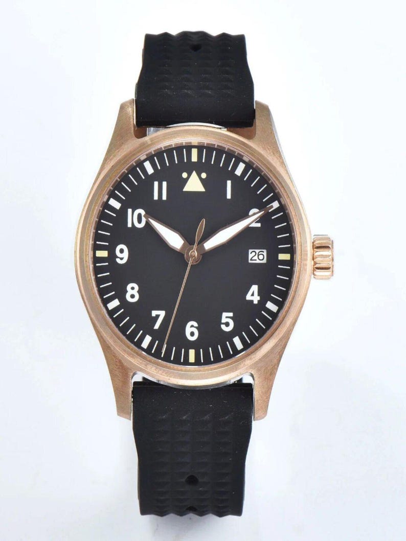 May include: A bronze-colored wristwatch with a black face and white numerals. The watch has a black rubber band and a date display at the 3 o'clock position. The watch hands are white and the second hand is bronze.
