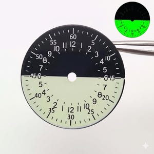 May include: A black and white watch dial with a luminescent lower half. The dial features numbers and markings for timekeeping, with a small hole in the center. A smaller, illuminated version is in the upper right.