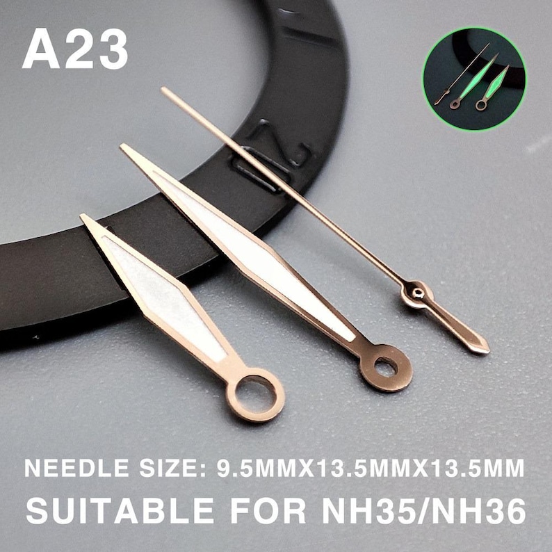 Op de afbeelding: Gouden en witte horlogewijzers, met een cirkelvormige opening aan de basis van twee wijzers. De tekst "A23" staat linksboven. De tekst "NEEDLE SIZE: 9.5MMX13.5MMX13.5MM SUITABLE FOR NH35/NH36" staat onderaan.