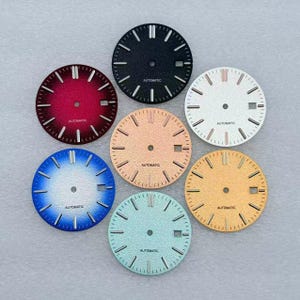 Pode incluir: Sete mostradores de relógio circulares em preto, vermelho, prata, azul, verde claro, ouro rosa e ouro. Cada mostrador apresenta marcadores de hora prateados, um orifício central para os ponteiros e uma pequena janela de data retangular.
