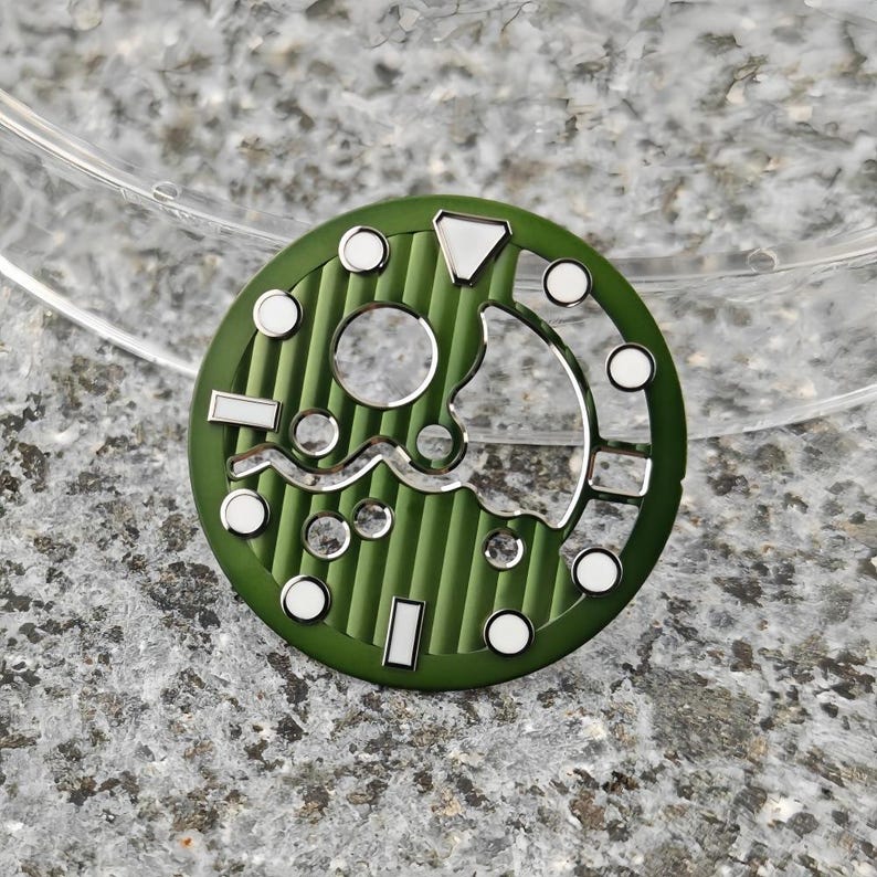 May include: A green watch dial with a textured, striped pattern. The dial features silver-colored cutouts and white circular and rectangular markers. The design includes a wave-like silver accent and a triangular marker.