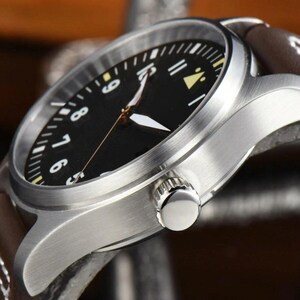 May include: Close-up of a stainless steel wristwatch with a black face and brown leather band. The watch features white and yellow hour markers and hands. The watch's crown is visible on the side.